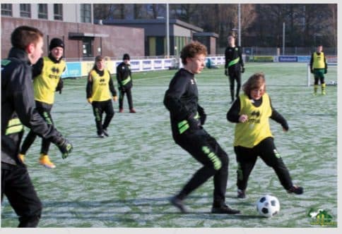 Kids in ADO Den Haag community bibs training with a football on a frosty pitch in The Hague