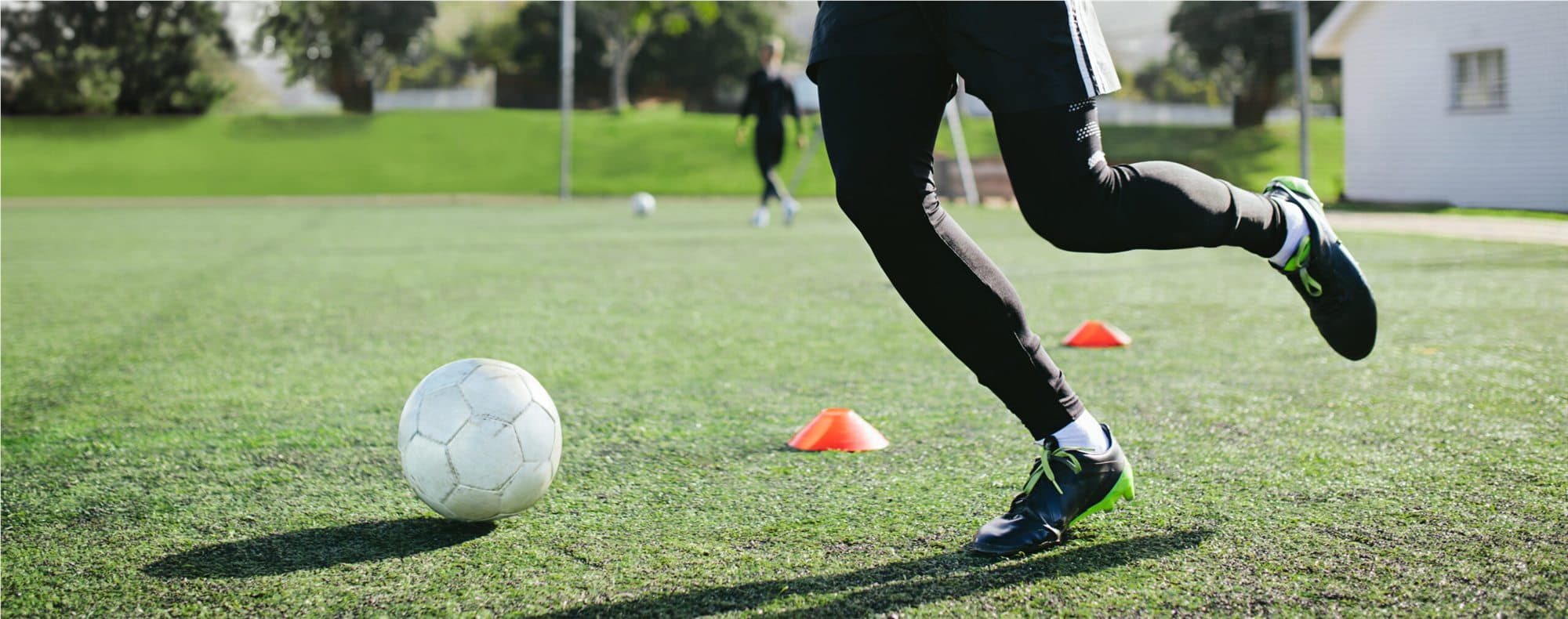 Young player dribbling a well-used football during a training session on a grass pitch